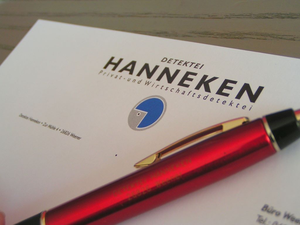 Ein roter Kugelschreiber liegt auf einer Visitenkarte der Hanneken Detektei.